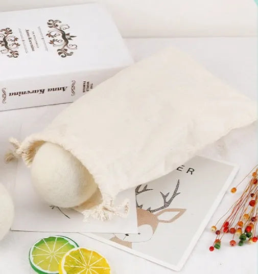Assorted sized wool drying balls next to a beige cotton drawstring storage bag on a wooden surface.