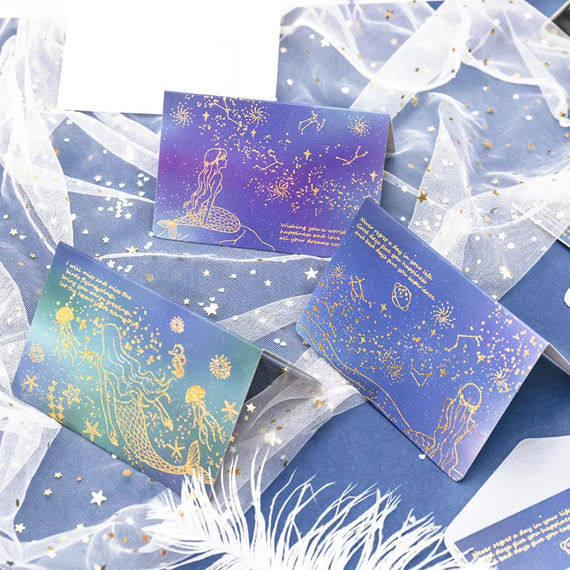 Set of three gilded greeting card envelopes in galaxy colour designs on a dark background.