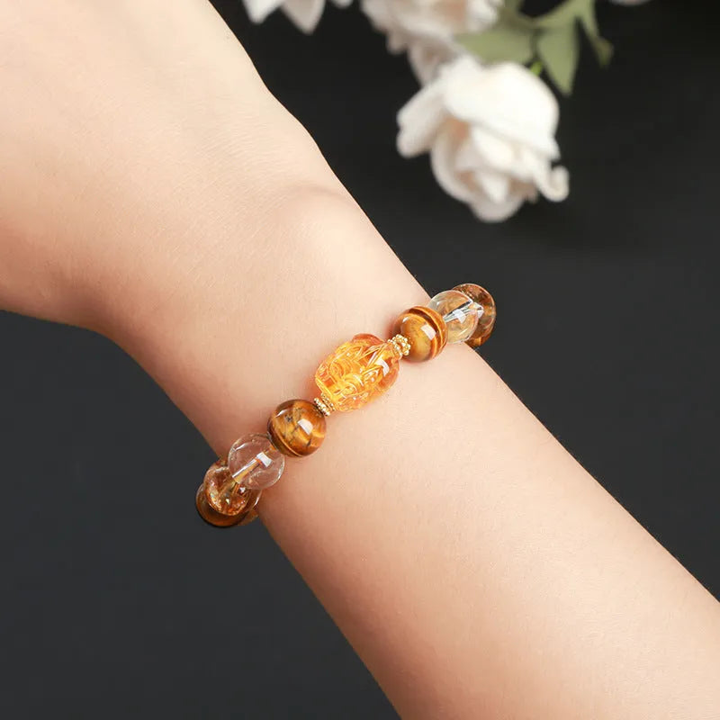 Natural yellow tiger's eye and citrine bracelet with 10mm round beads and a silver pi xiu charm on a wrist.