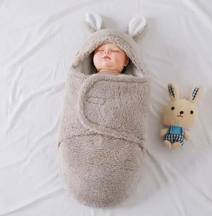 A baby wearing a soft grey fleece sleeping bag with hook-and-loop shoulder straps.
