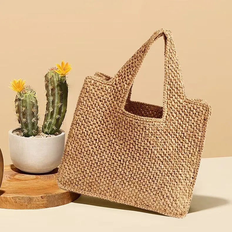 Khaki coloured woven straw tote bag with double straps showing open top and horizontal square shape.