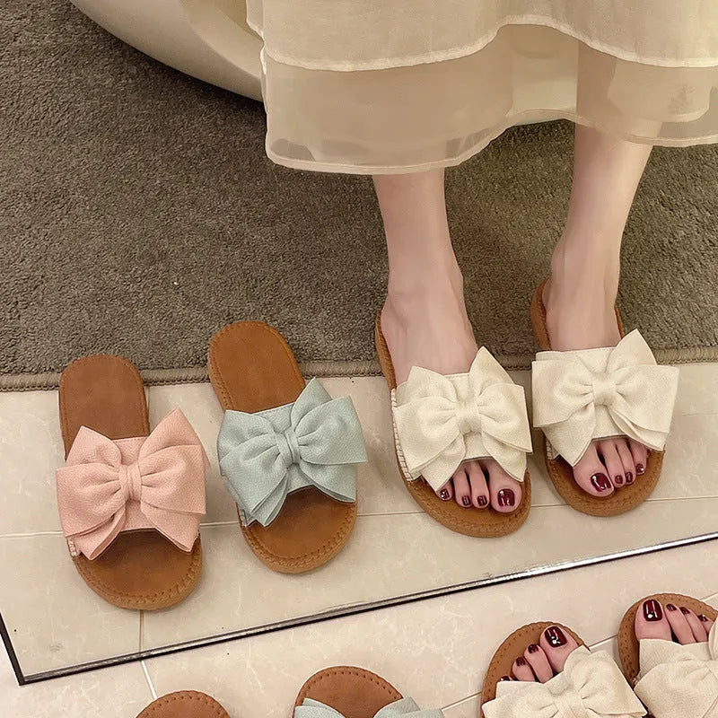 Women's beige slip-on sandals with a suede cloth upper, soft rubber sole, and decorative bow.