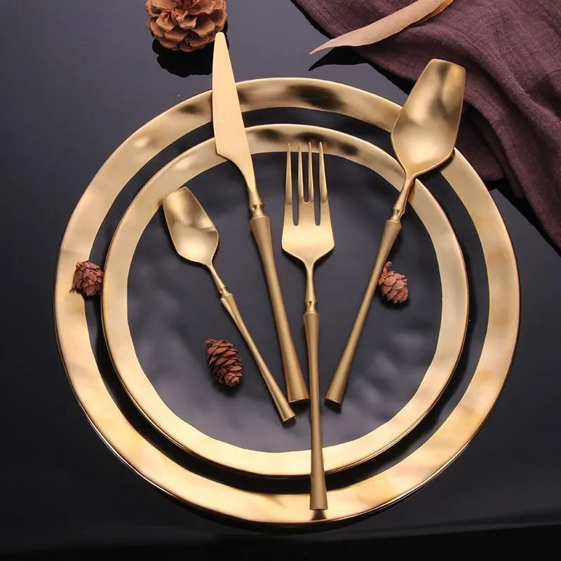 Stainless steel cutlery set with gold finish including knife, fork, spoon, and teaspoon on table