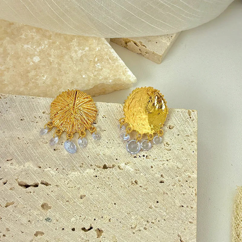 A pair of geometric gold metal earrings with round details on a white background.