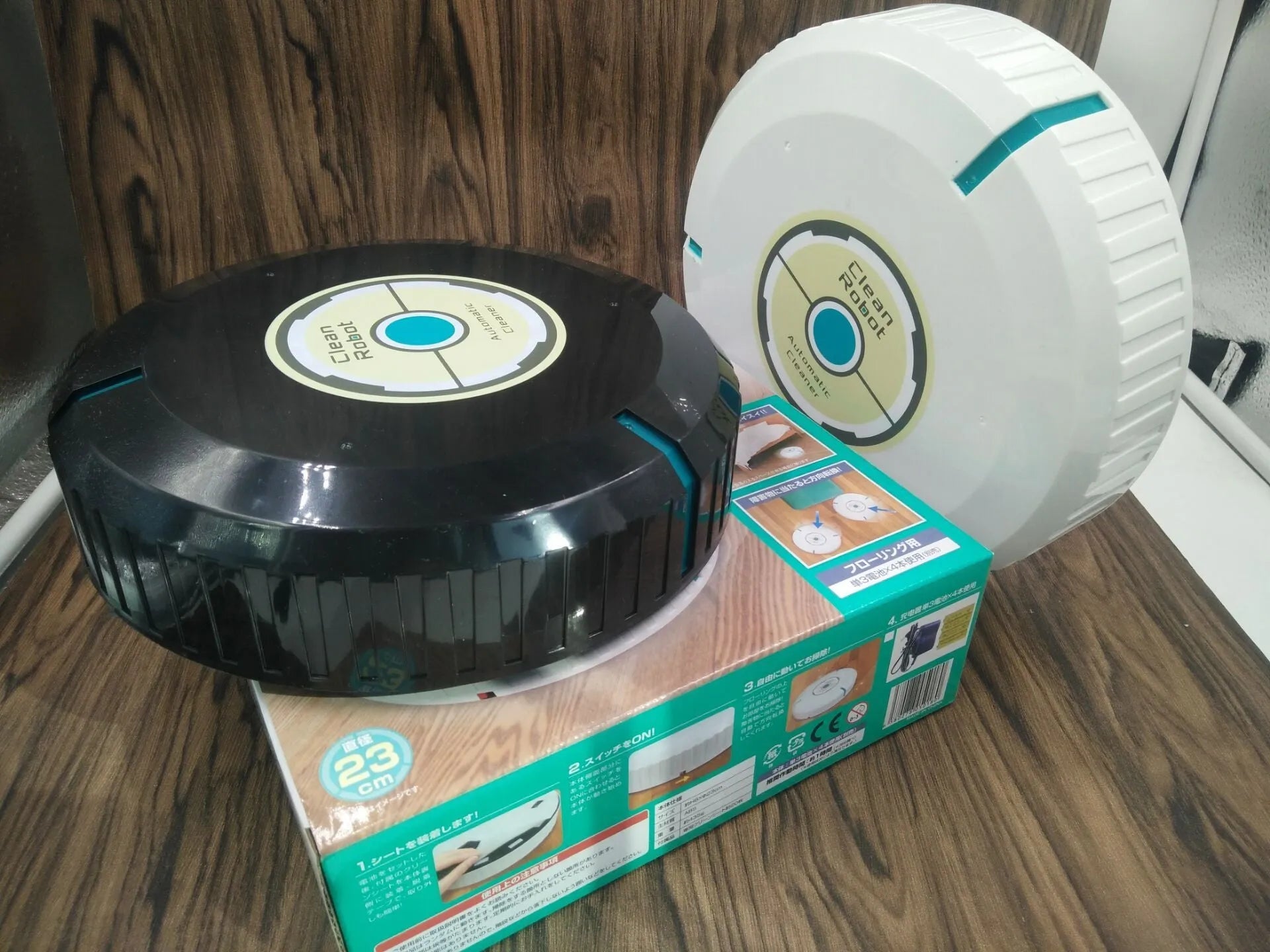 Black or white automatic robot vacuum cleaner with wide cleaning head on wooden floor.