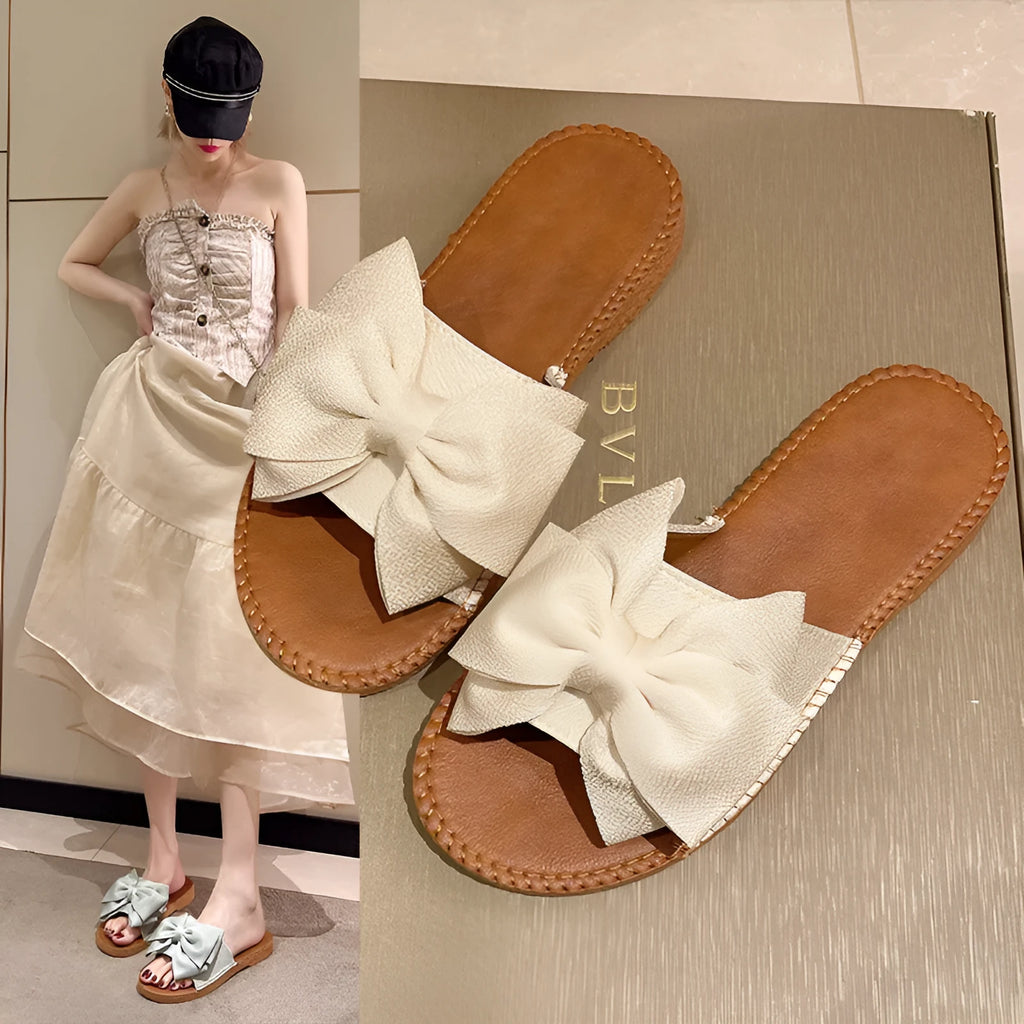 Women's beige slip-on sandals with a suede cloth upper, soft rubber sole, and decorative bow.