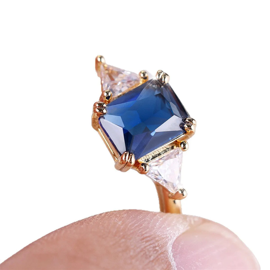 Gold sapphire blue rectangular copper ring for women on a plain background