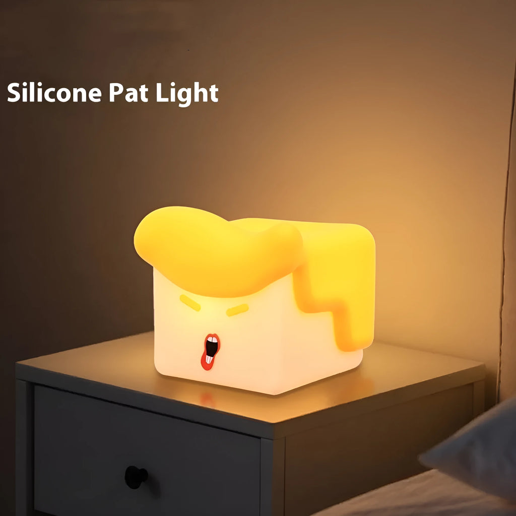 Yellow soft silicone pat lamp with USB charging port on a wooden table showing night light glow