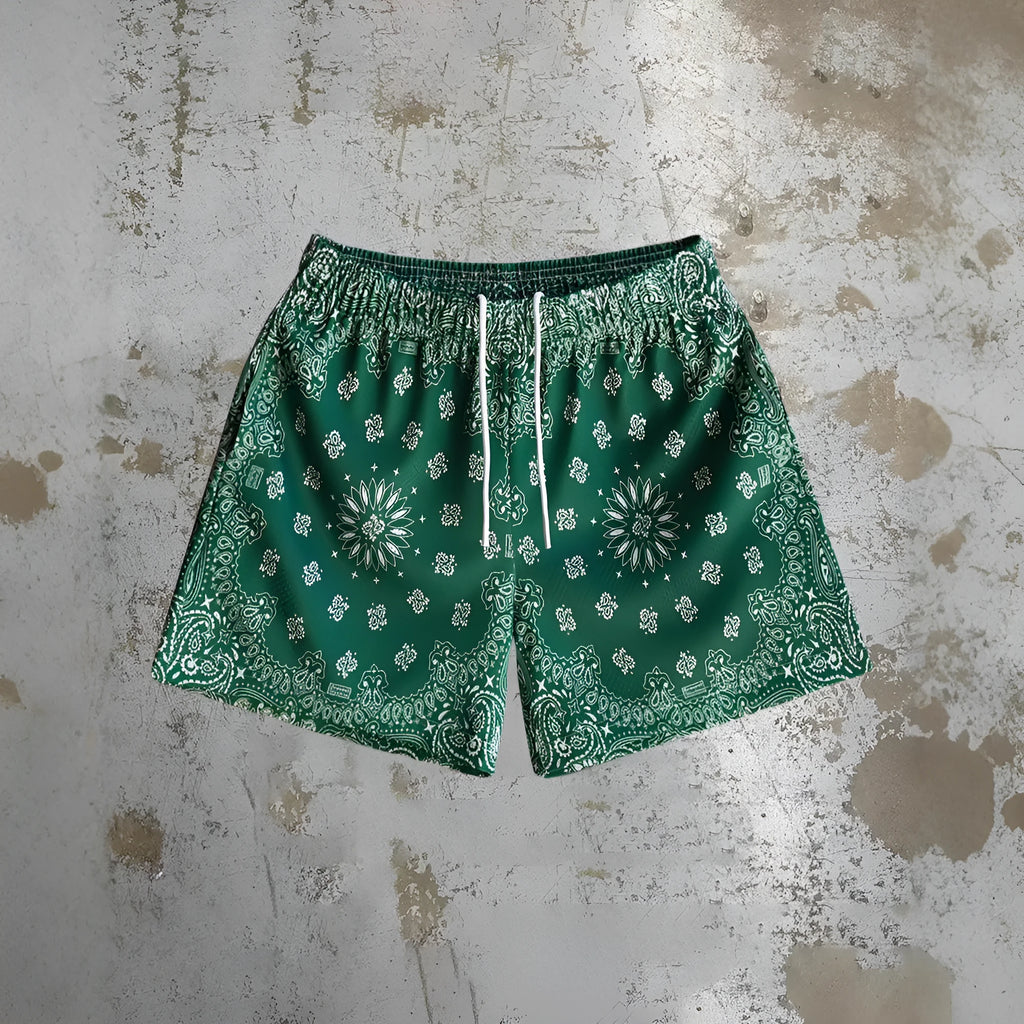Man's loose blue digital print beach shorts with elastic waistband on a sandy background.