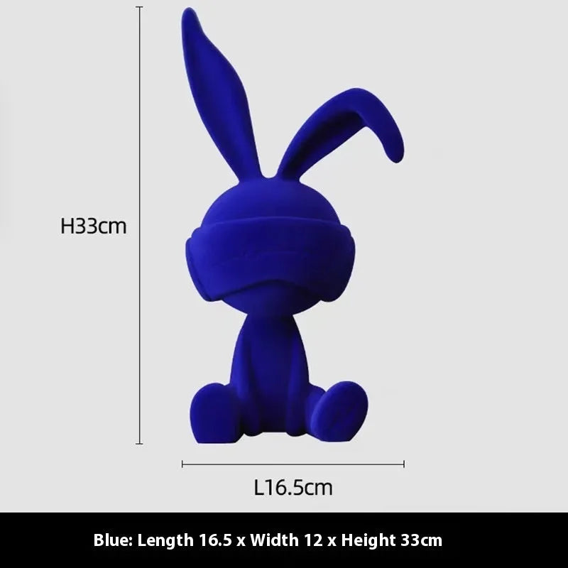 Green resin blindfold rabbit table ornament with suede details on a wooden shelf.