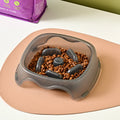 A blue plastic slow-feeder dog bowl on a wooden floor.