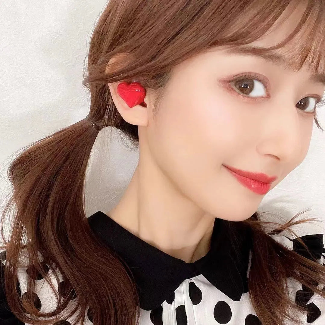 Red and pink heart-shaped wireless Bluetooth in-ear headphones with charging cable.