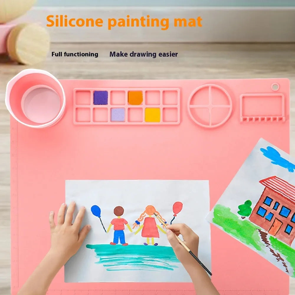 Light blue silicone painting mat with two bowl compartments on a wooden table.