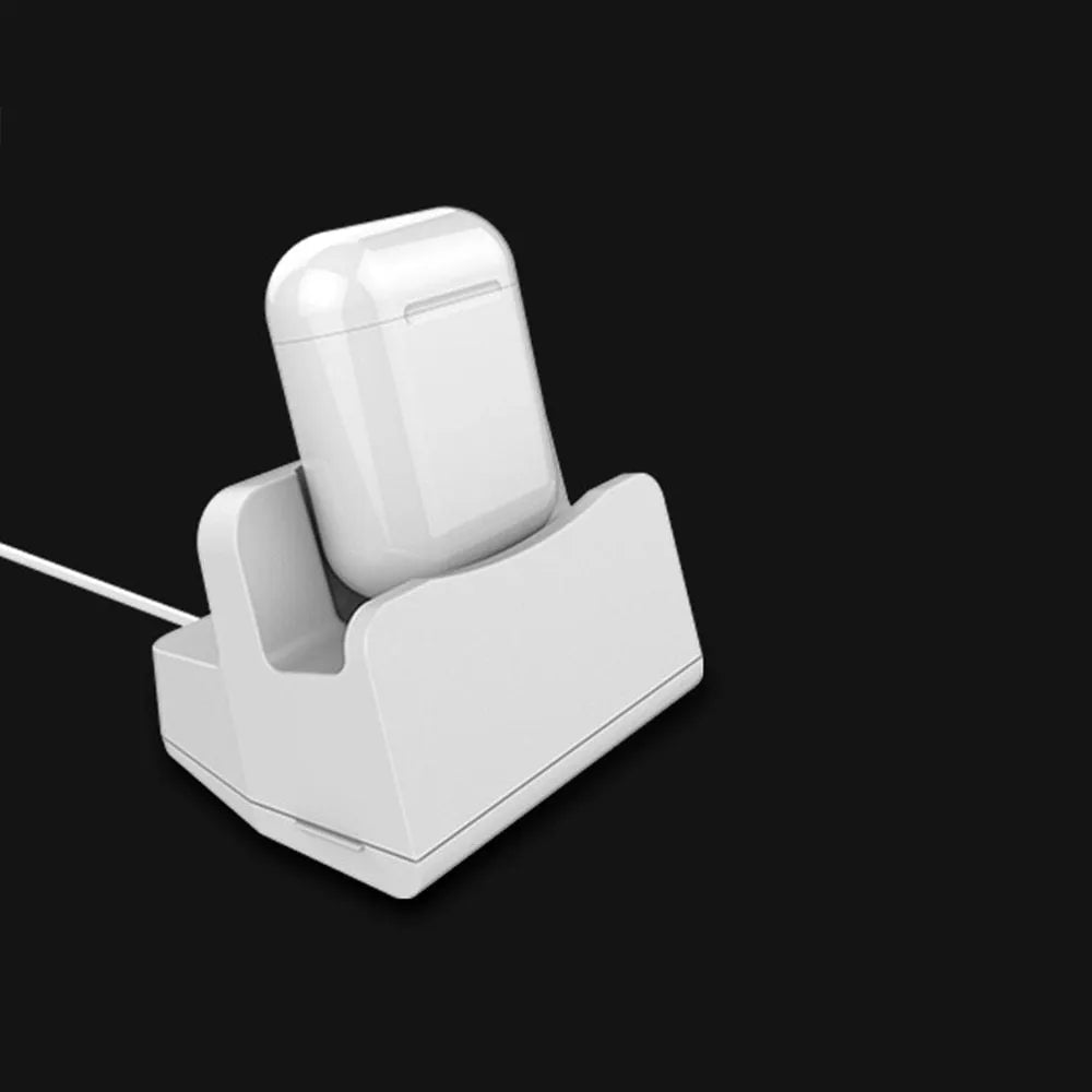 White headphone charging base station on a desk, holding a pair of over-ear headphones.