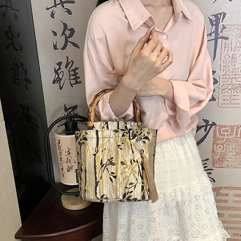 Beige polyester women's handbag with bamboo handles and pendant on neutral background