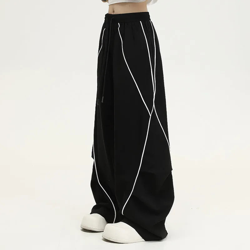 Black trousers with vertical stripes and pleated detail on the legs, showing a loose wide-leg fit.