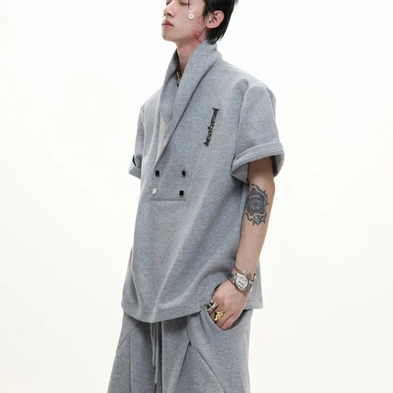 Men's dark grey v-neck sports jacket with padded shoulders and metal details, worn with matching shorts.