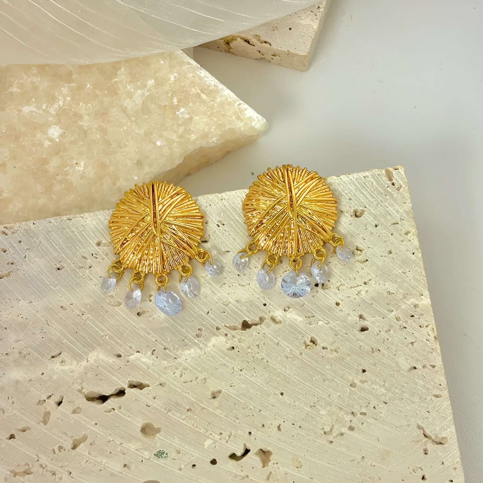 A pair of geometric gold metal earrings with round details on a white background.