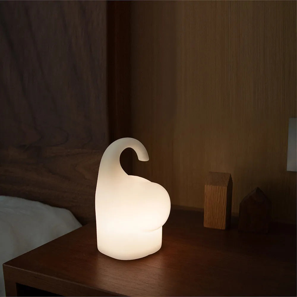 White silicone elephant-shaped night light with a warm glow, placed on a wooden bedside table.