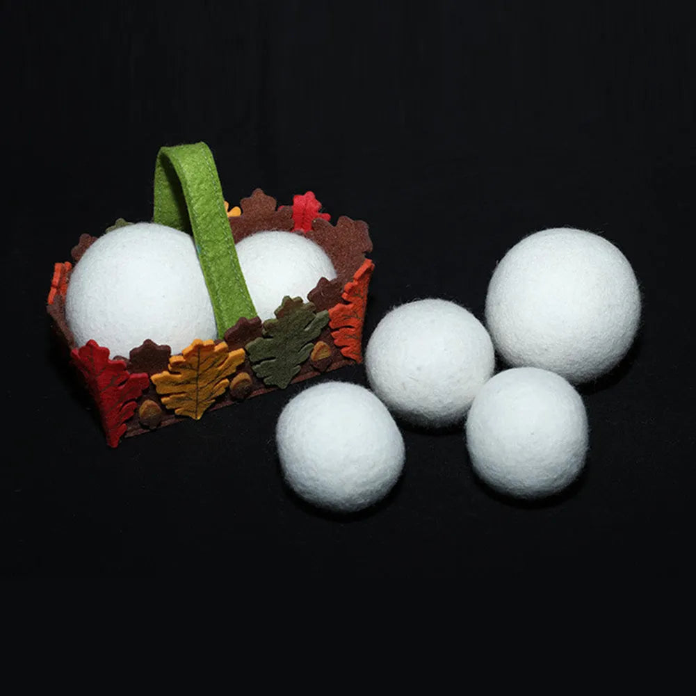 Assorted sized wool drying balls next to a beige cotton drawstring storage bag on a wooden surface.