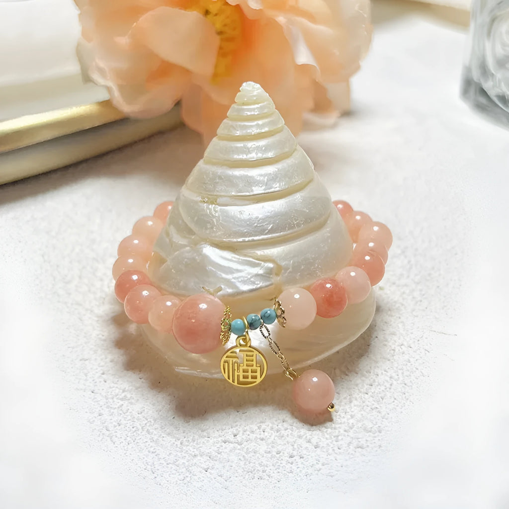 Close-up of a women's pink natural stone and alloy charm bracelet on a wrist, showing adjustable fastening.
