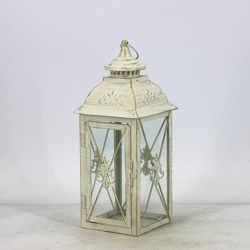 Black and white wrought iron floor standing storm lantern with tempered glass panels on a patio.