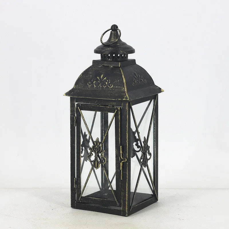Black and white wrought iron floor standing storm lantern with tempered glass panels on a patio.