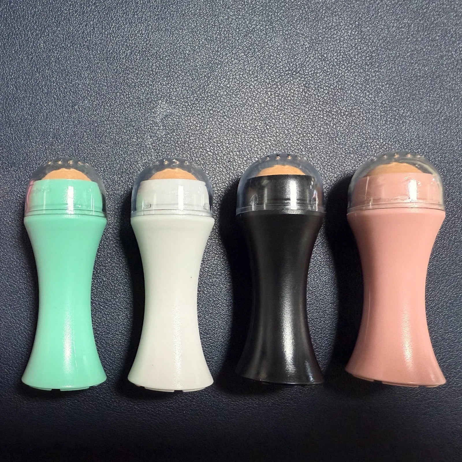 Volcanic stone portable roller for oily skin control in black, green, pink, and white.