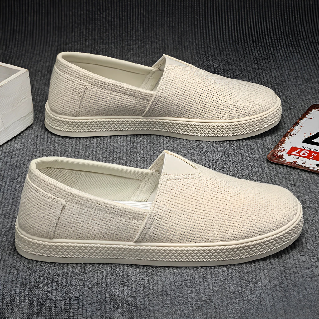 Men's beige canvas slip-on loafers with a round toe and shallow cut on a plain background.
