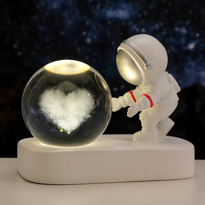 Small clear resin ball night light with glowing astronaut and galaxy scene inside on dark surface