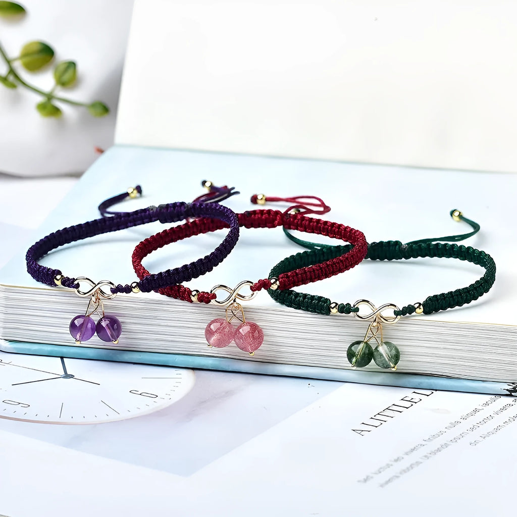 Women's bracelet with a natural strawberry quartz cherry charm on a black elasticated string.
