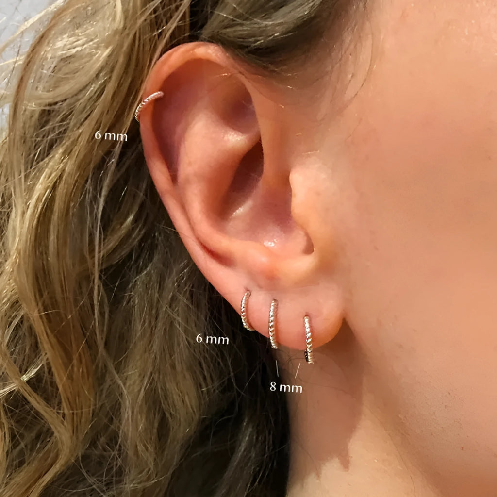 Close-up of twisted S925 sterling silver round ring earrings in gold colour on a plain background.