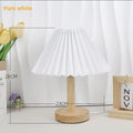 Vintage red pleated umbrella-shaped bedside lamp with remote control on a wooden nightstand.