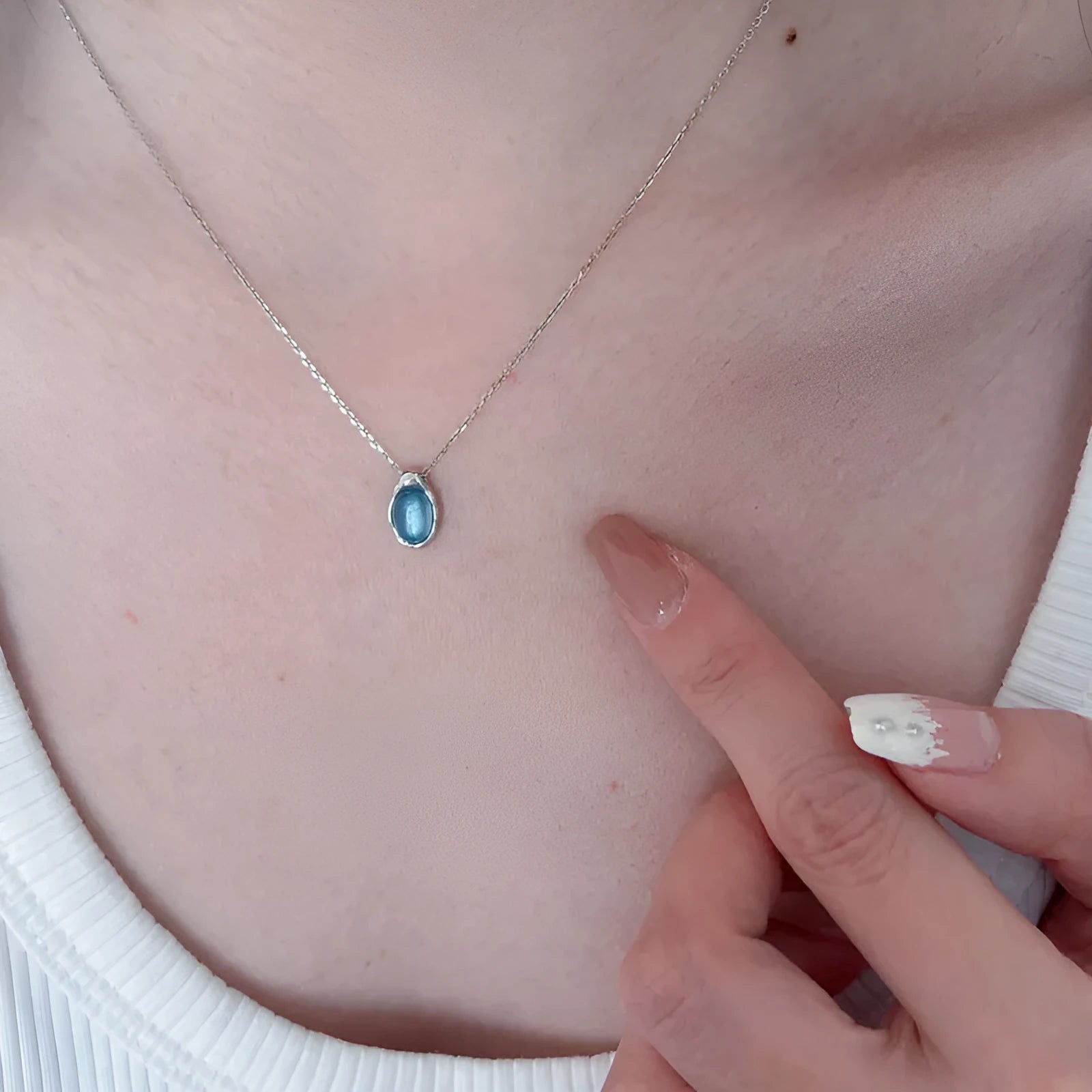 Close-up of a navy blue geometric water drop pendant on a platinum-colour adjustable cross chain necklace.