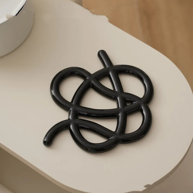 Ceramic heat proof mat in irregular shape on a table, shown in bright black colour.