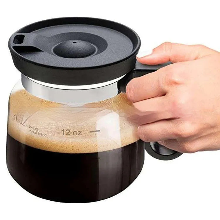 Transparent borosilicate glass stovetop coffee maker with black silicone cover on a hob.