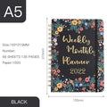 A5 spiral notebook open on a desk showing one of ten available artistic cover designs.