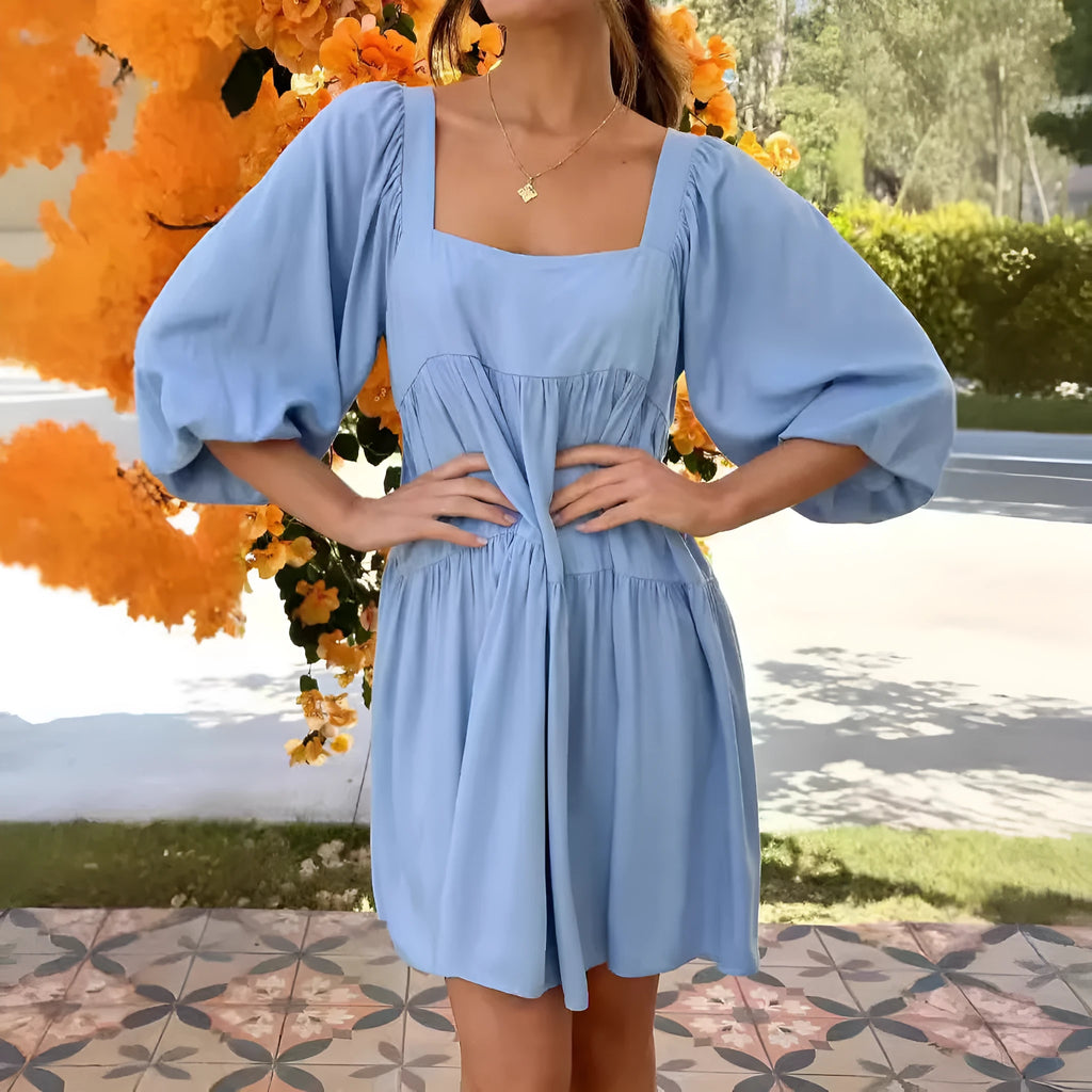 A light blue children's backless dress with a square collar, puff sleeves, and an A-line skirt on a hanger.