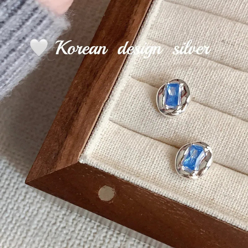 Women's sterling silver oval earrings with heart-wrapped design and blue diamond accents on silver background