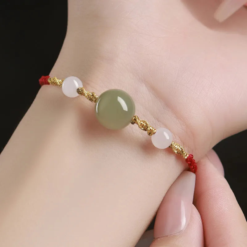 Hand-woven red rope bracelet with Hetian jade beads and intricate charm detailing.