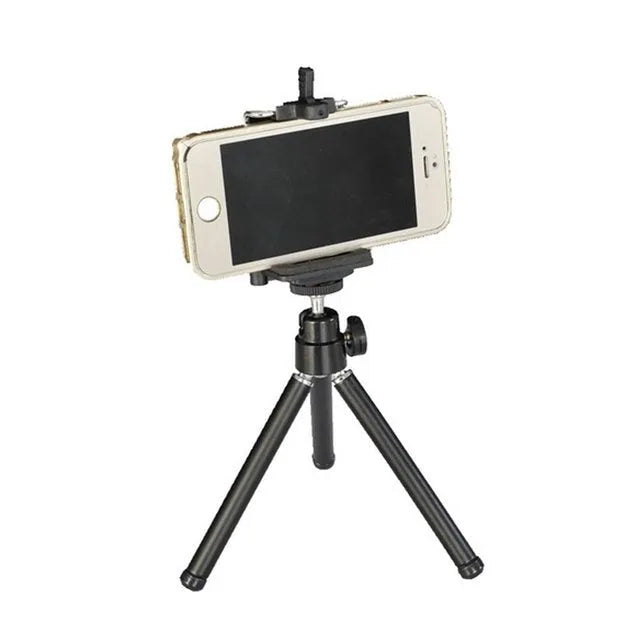 Black mini desktop camera tripod with extended legs and a U-shaped phone clip attached, on a white background.