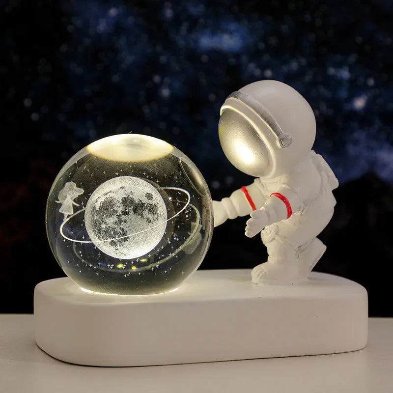 Small clear resin ball night light with glowing astronaut and galaxy scene inside on dark surface