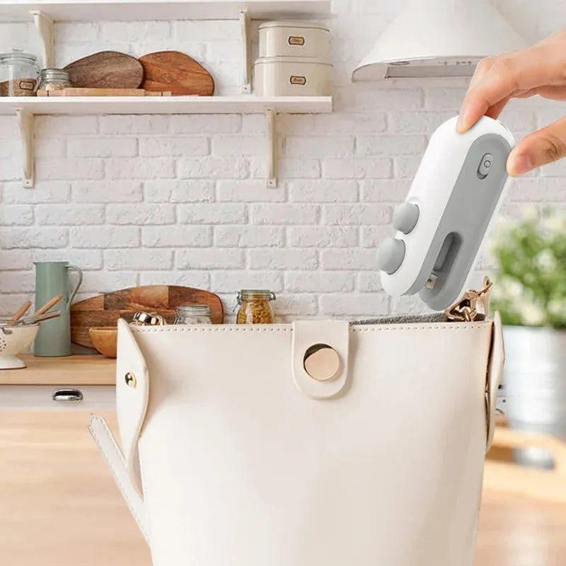 Blue and white handheld USB rechargeable heat sealer for sealing food storage bags on a kitchen counter.