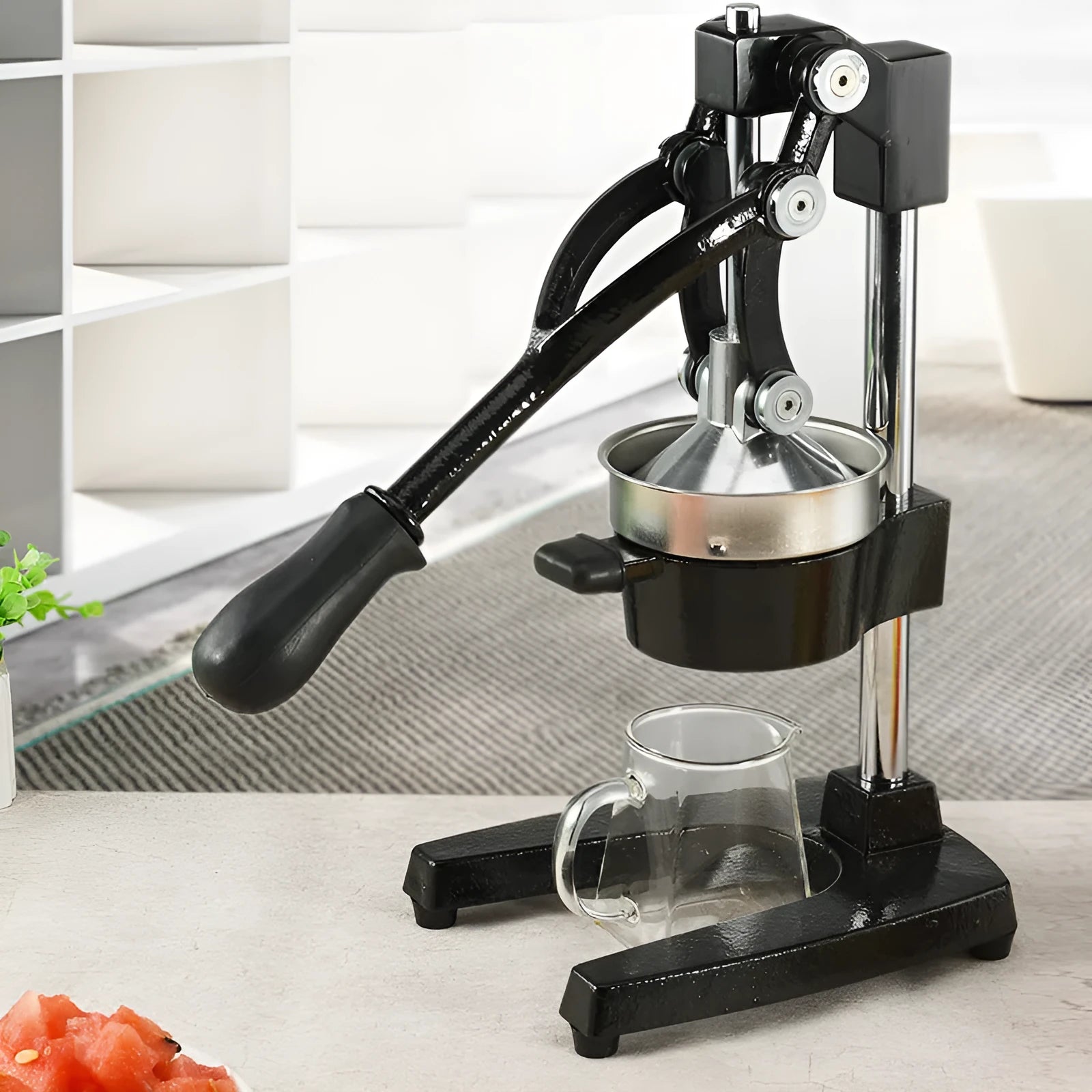 Black cast iron manual citrus juicer with stainless steel strainer on a kitchen counter.