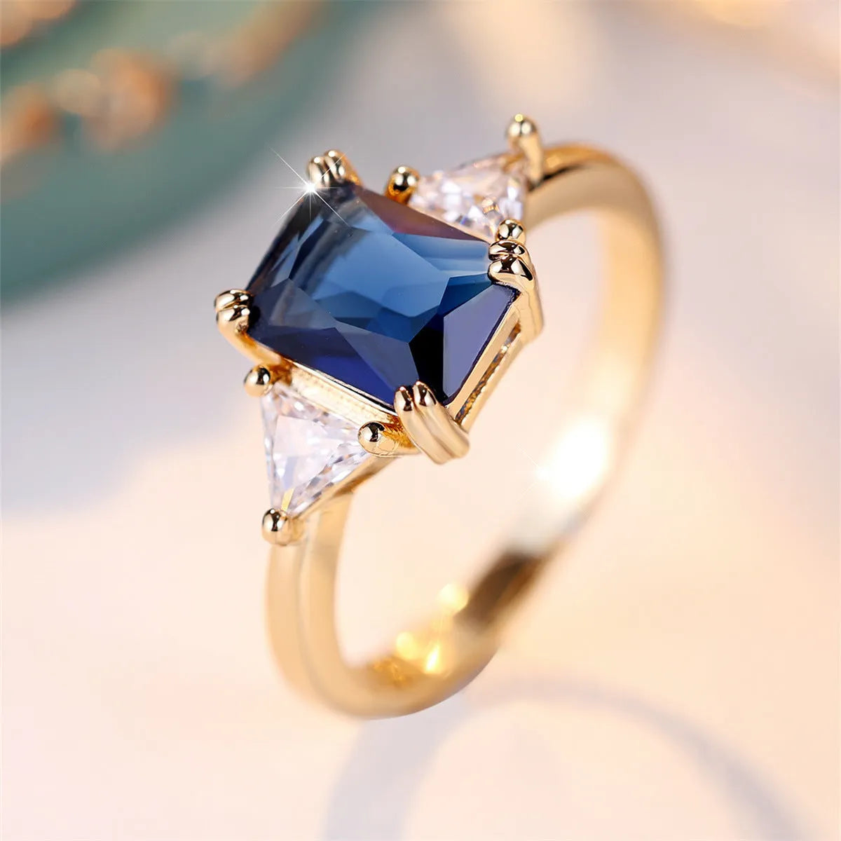 Gold sapphire blue rectangular copper ring for women on a plain background