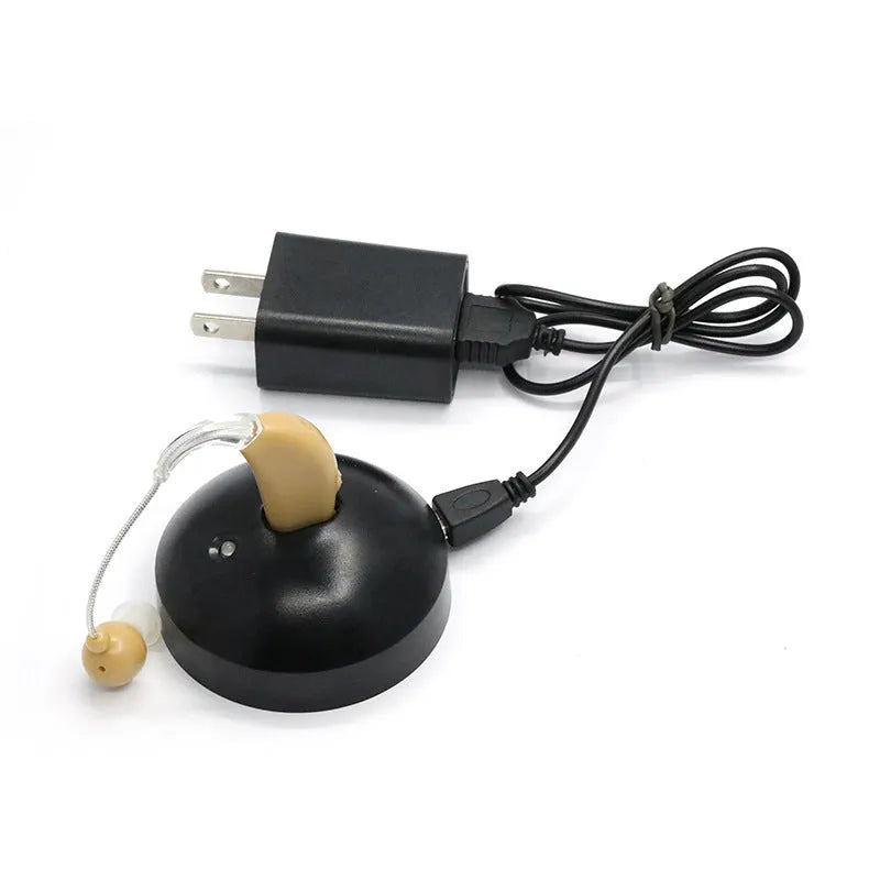 Black silicone rechargeable hearing aid amplifier with charging cable on a table.