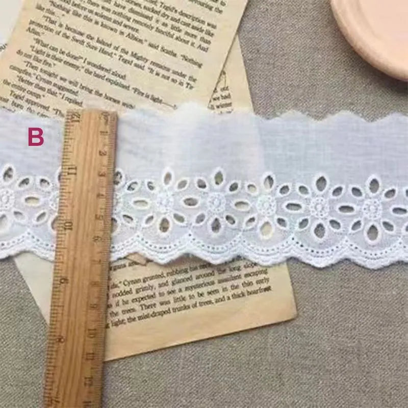 Cotton embroidered lace trim on roll showing cutout pattern, with width measurement examples