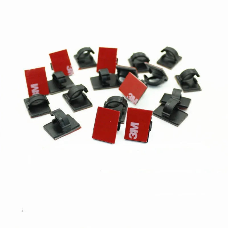Black and white plastic self-adhesive cable clamps for car wire management on a clean surface.