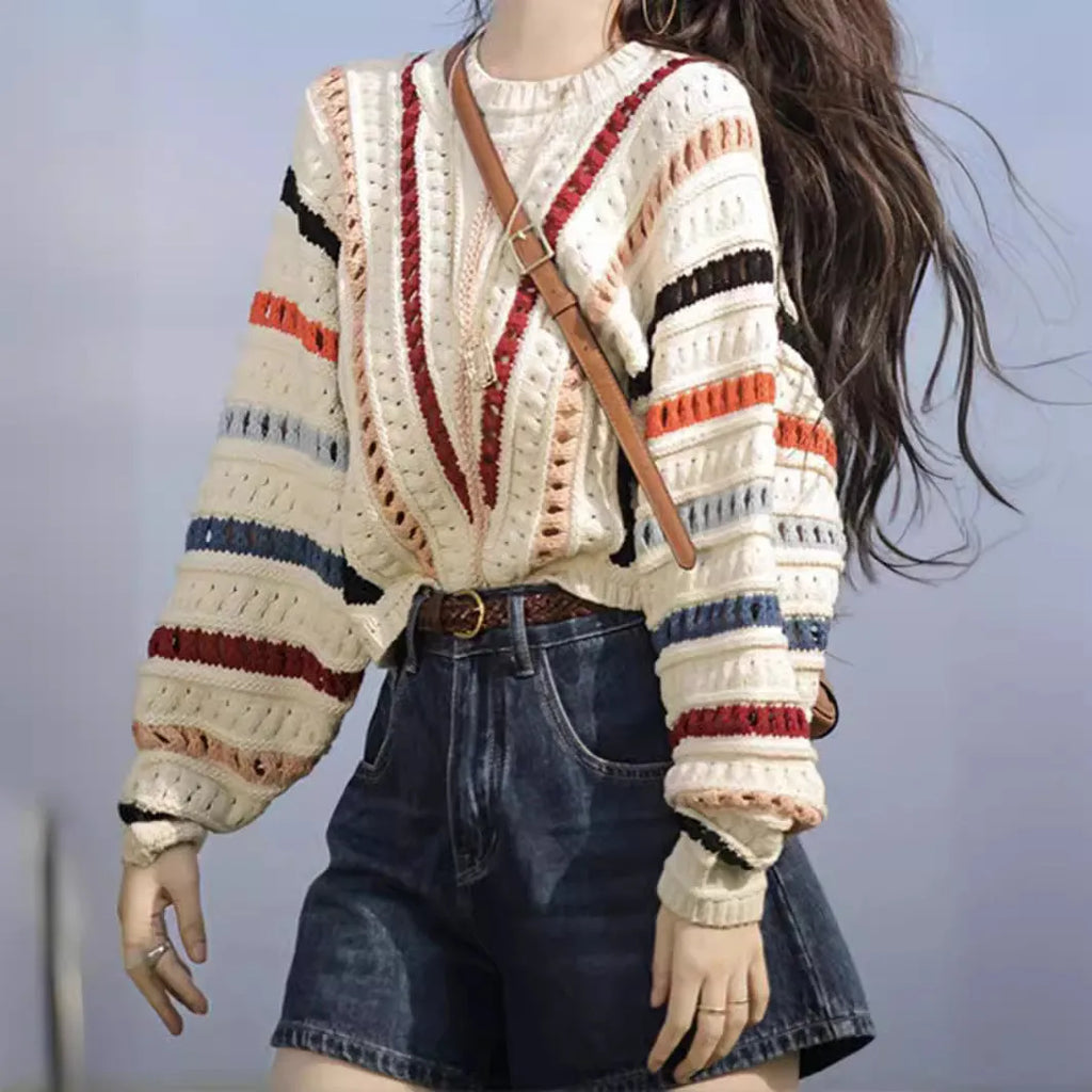 A woman's rainbow striped loose knit sweater with batwing sleeves on a hanger.