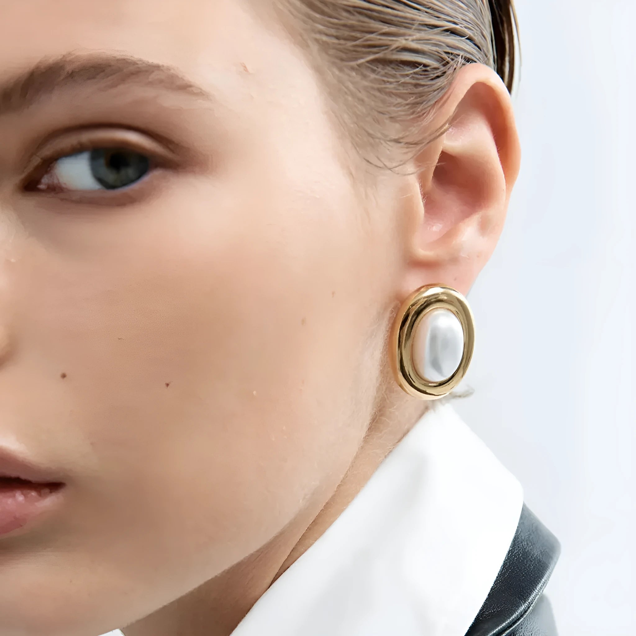 Close-up of a pair of round stainless steel stud earrings with a vintage-style pearl detail on a neutral background.